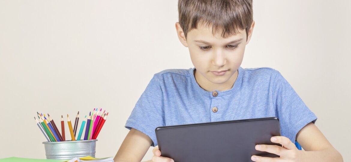 Kid with tablet computer sitting at table with books notebooks