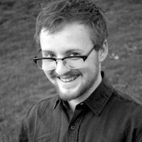 person with glasses and short hair and beard and light skin smiling, black and white photo