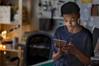 A teen checks social mboy plays a game in his room on a digital tablet at night.