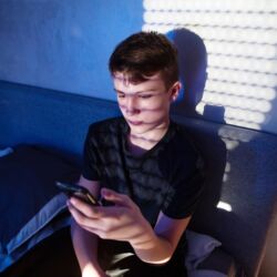 teenager boy sitting in his bedroom using cell phone