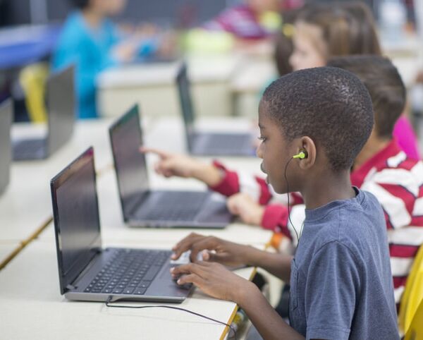 A multi-ethnic group of elementary age children are working on individual laptops in the computer lab.